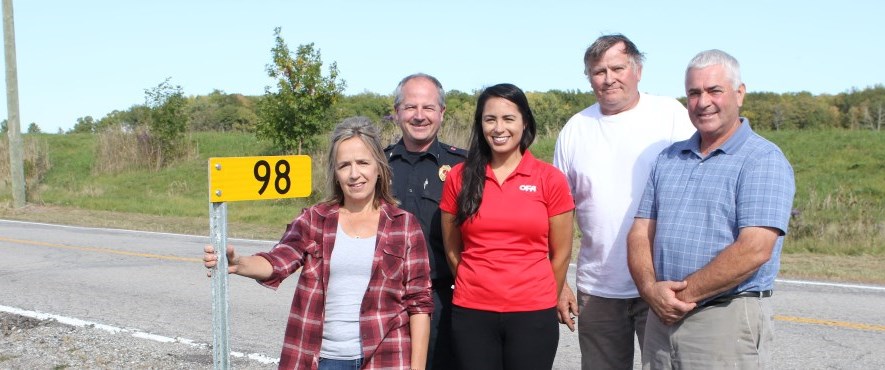 people standing next to farm 911 sign on road