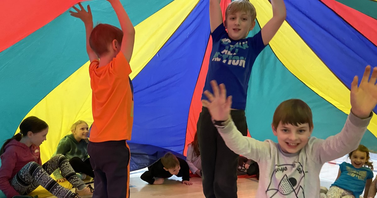 children underneath rainbow coloured parachute