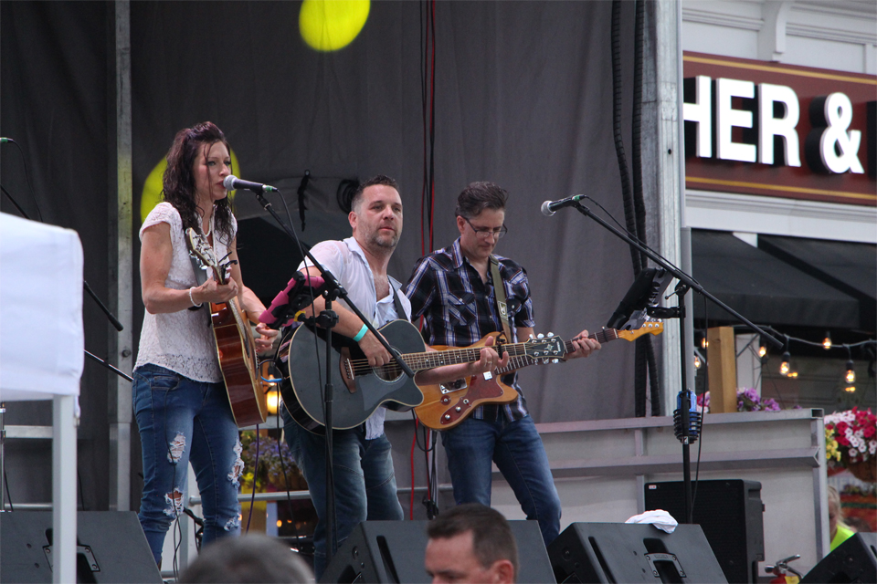 band on stage, one woman and two men singing and playing guitar