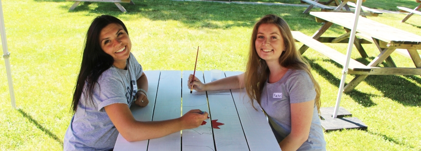 Two girls painting a picnic table for Canada day